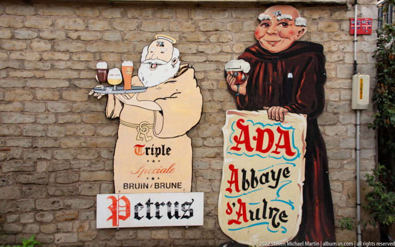 Two painted beer signs on brick showing monks with glasses and the names Petrus and Abbaye d'Aulne.