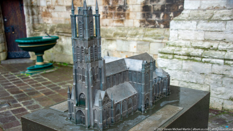 Dark metal model of a Gothic church with tall tower, nave, transepts, and buttressed side walls.