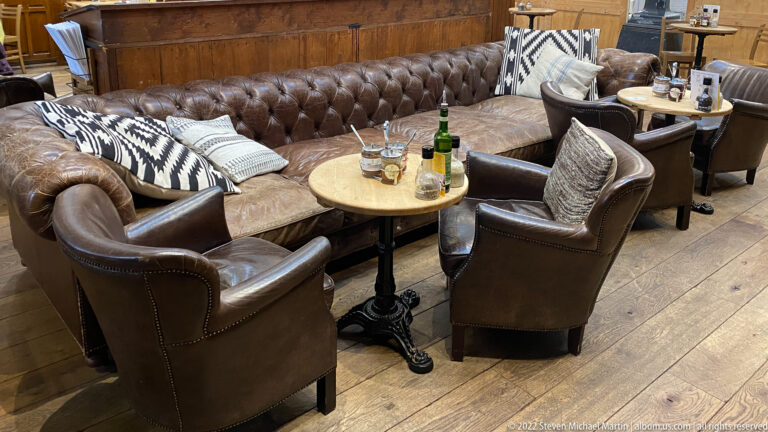 Brown leather armchairs and tufted sofa around small tables with drinks in a warm wood-paneled lounge.