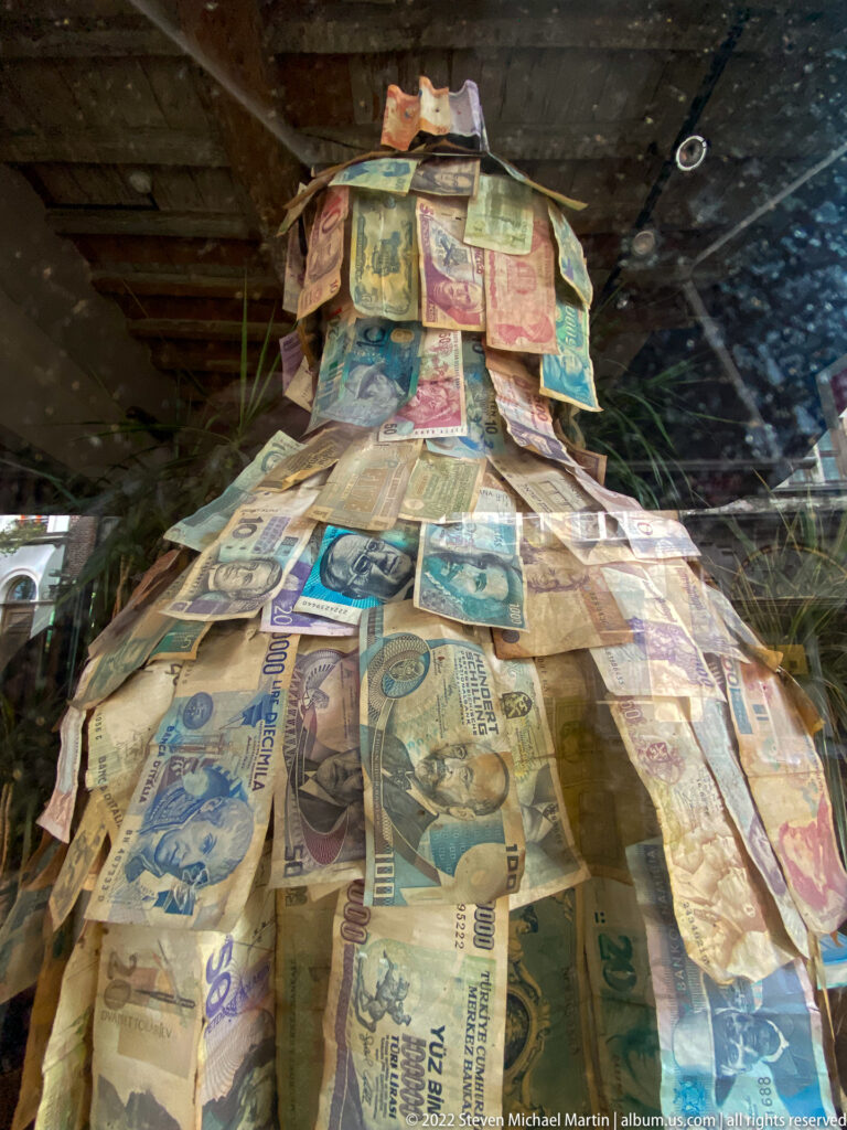 Dress-shaped artwork made from overlapping multicolored banknotes displayed behind glass.