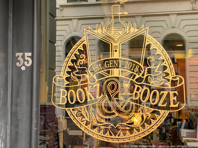 Gold Bookz & Booze window logo reading Est. Gent 2018, with book, bottle, foliage, and decorative lettering.