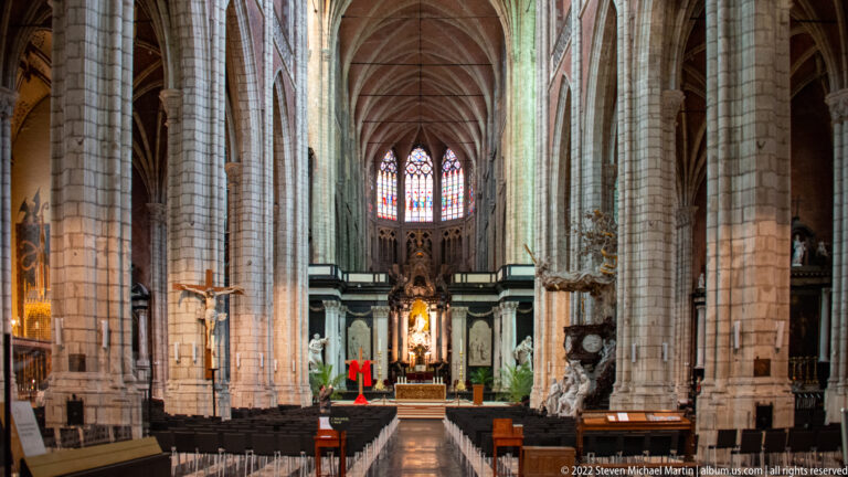Closer view down Saint Bavo's Cathedral nave toward the illuminated high altar beneath stained glass.