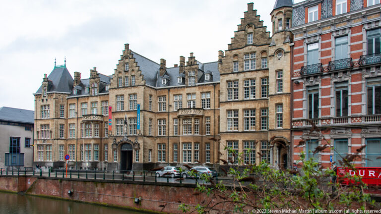 Historic Ghent townhouses with stepped gables and tall windows seen across a narrow canal-side edge.