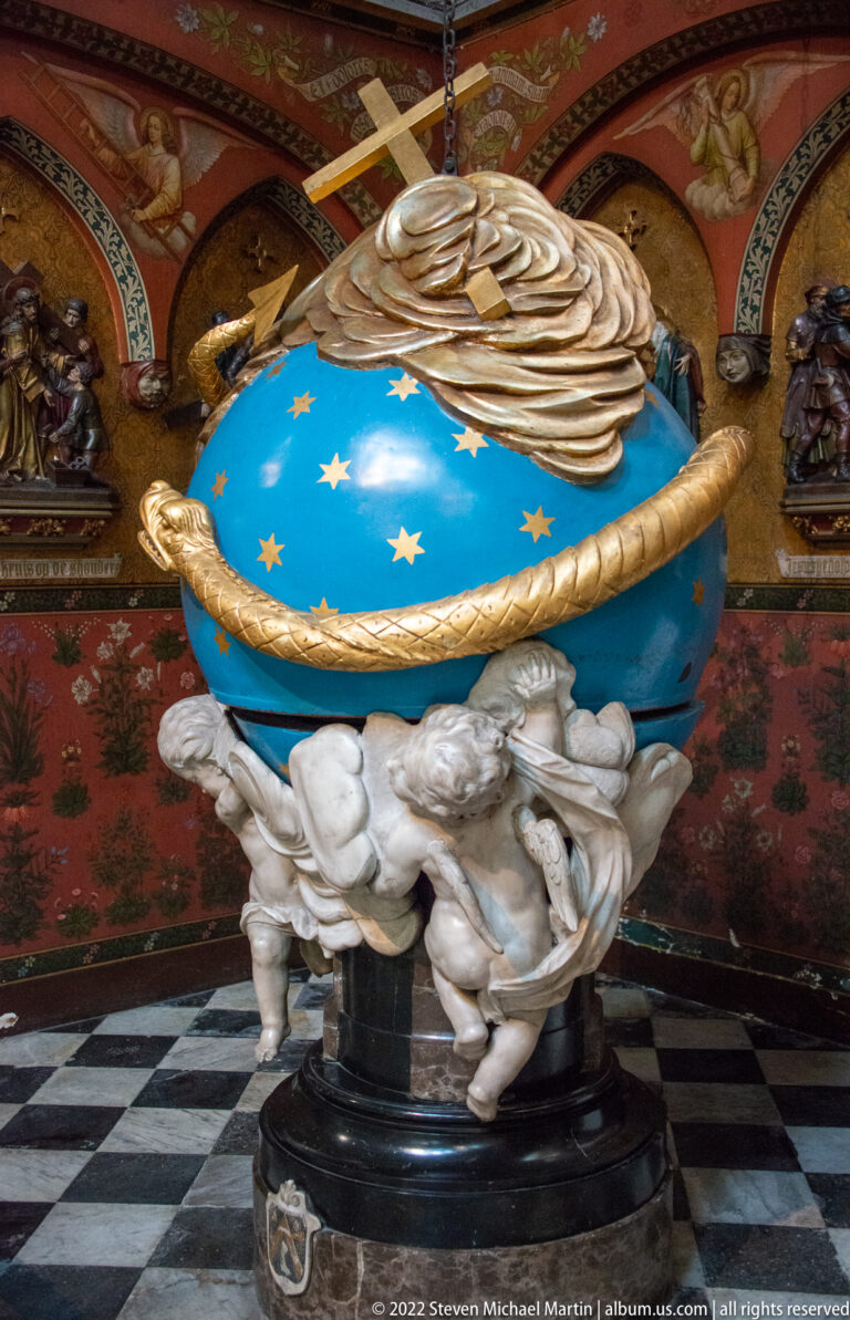 Bright blue globe with gold stars and ring, supported by sculpted putti in an ornate cathedral interior.