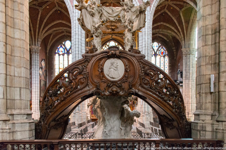 Curved carved wooden pulpit balustrade with an oval portrait medallion and pale sculpture above.