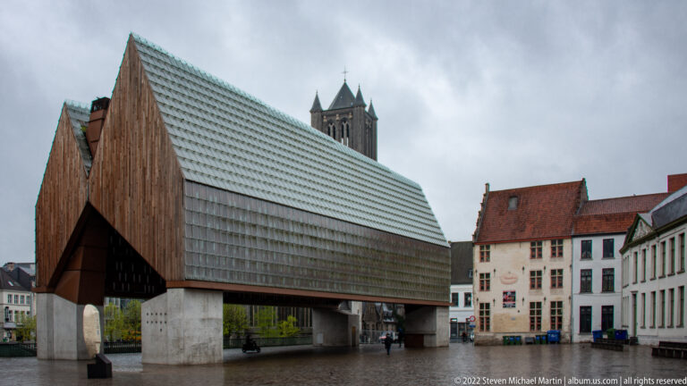 Ghent City Pavilion with steep timber-clad roof, glazed upper surface, and open concrete supports in the historic center.