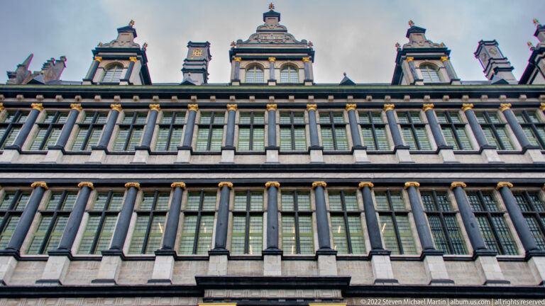 Upper historic façade with rows of tall windows, dark pilasters, gilded capitals, and decorative gables along the roofline.