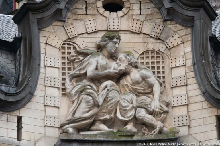 Stone sculptural group of a seated woman and reclining man set above an arched architectural opening.