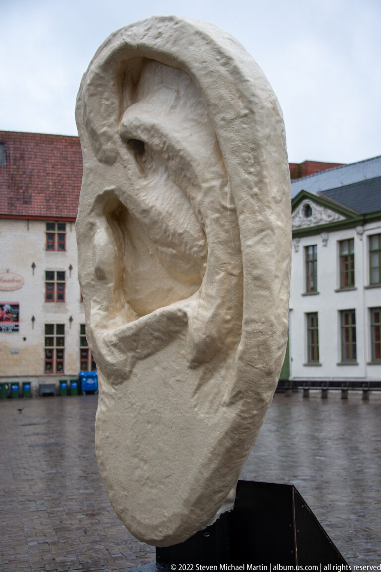 Abstract pale stone sculpture with a large hollowed circular form standing on a black base in a city square.