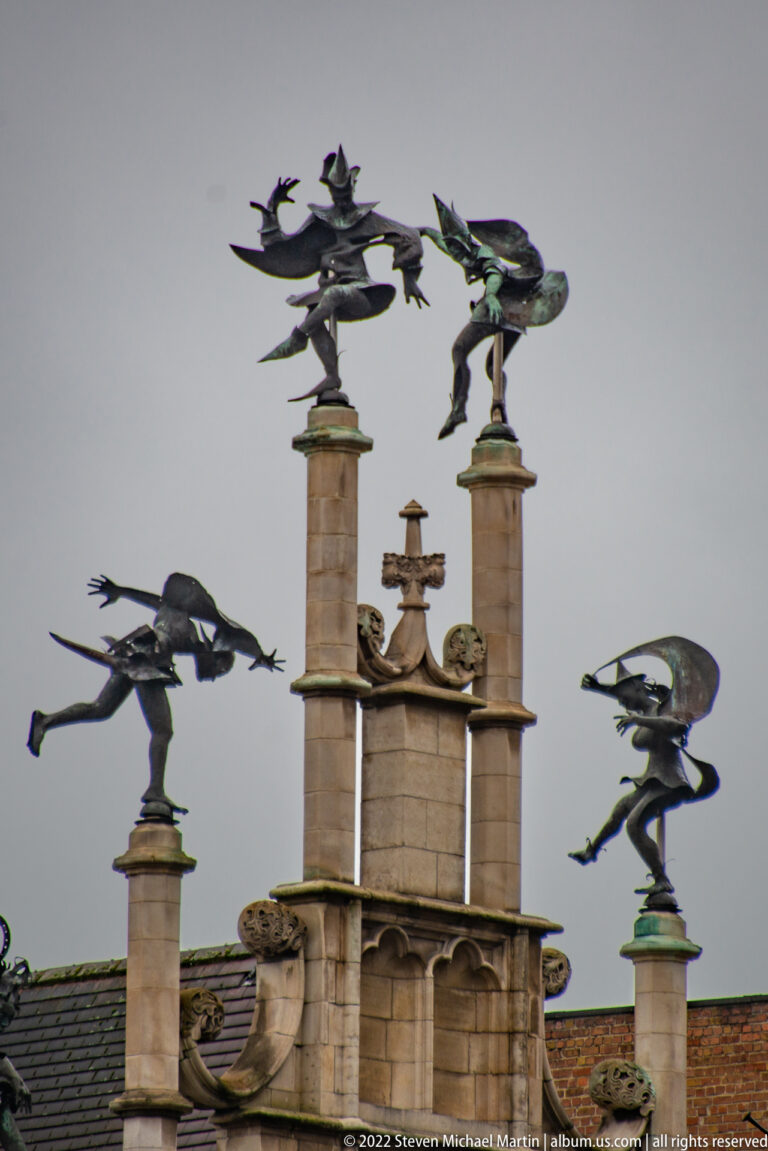 Dark winged metal figures perched on tall stone finials above a decorative historic roofline.