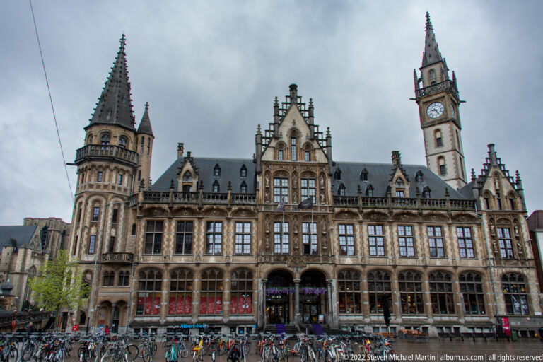 Former Ghent post office with ornate stone façade, turrets, clock tower, bicycles, and pedestrians at Korenmarkt.