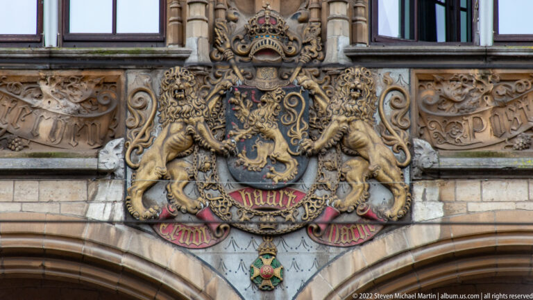 Crowned heraldic shield with two lion supporters and painted details carved above an arch on the former post office.