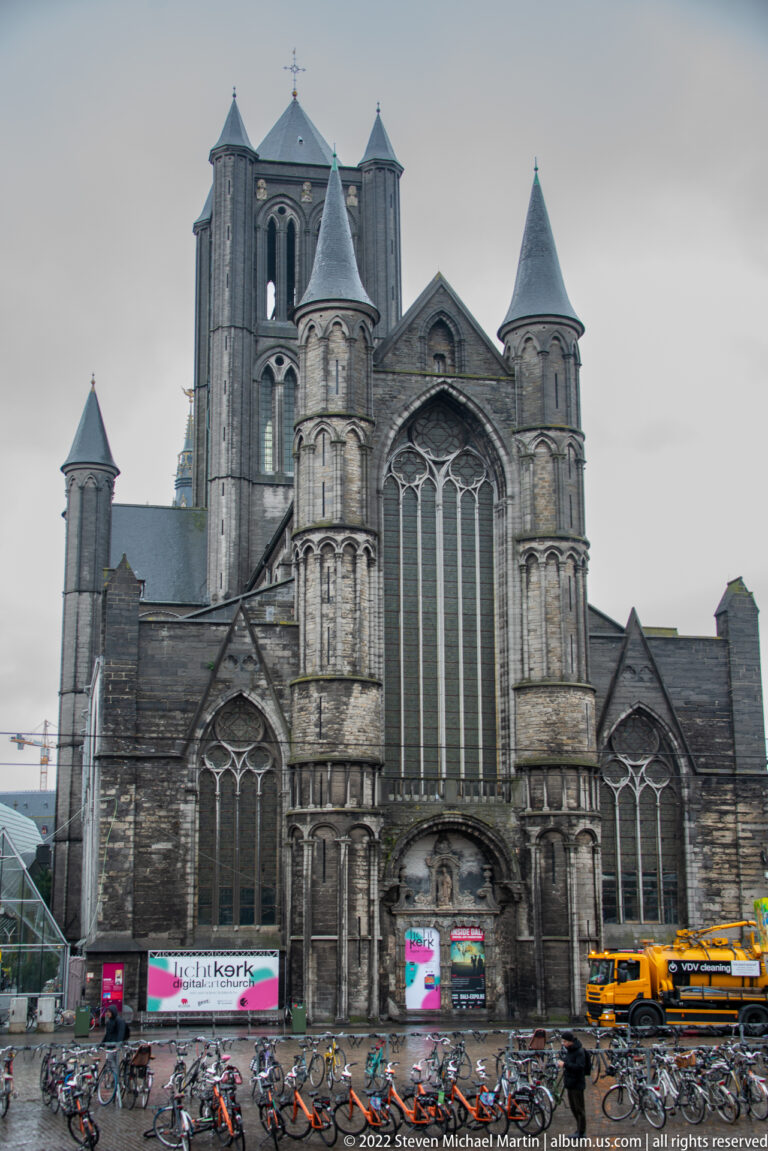 Saint Nicholas' Church façade with large Gothic window, corner turrets, central tower, bicycles, and street activity.