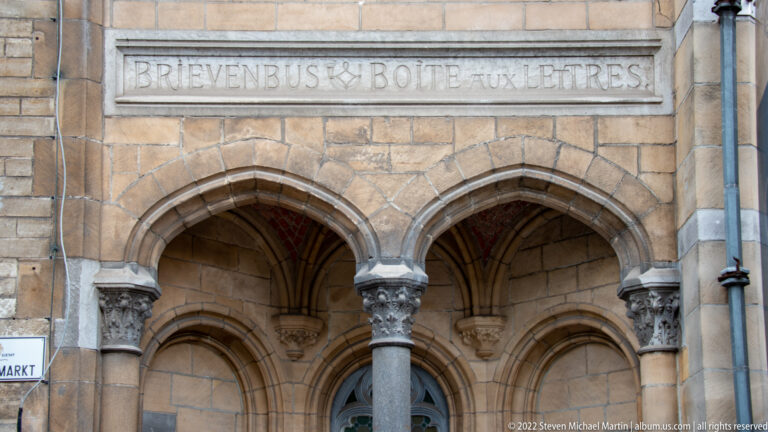 Two pointed stone arches on slender columns with carved capitals beneath a shallow inscription band.