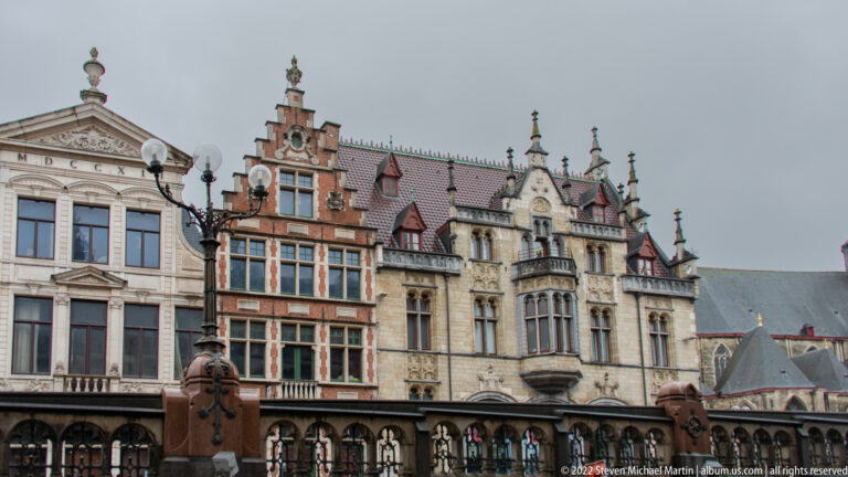 Decorated historic Ghent façades with stepped gables, projecting bays, stone balustrade, and tall lamp standards.