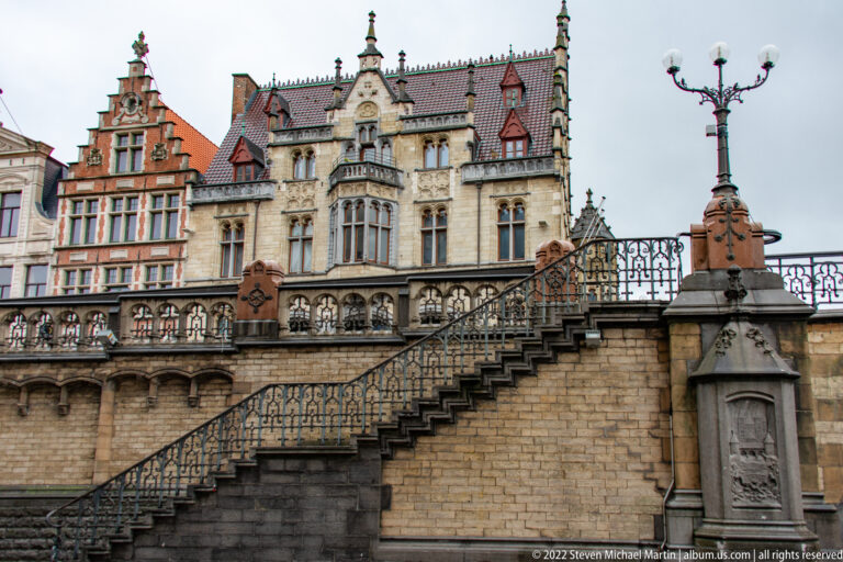Wide stone staircase with decorative iron railings leading toward an ornate gabled historic building.