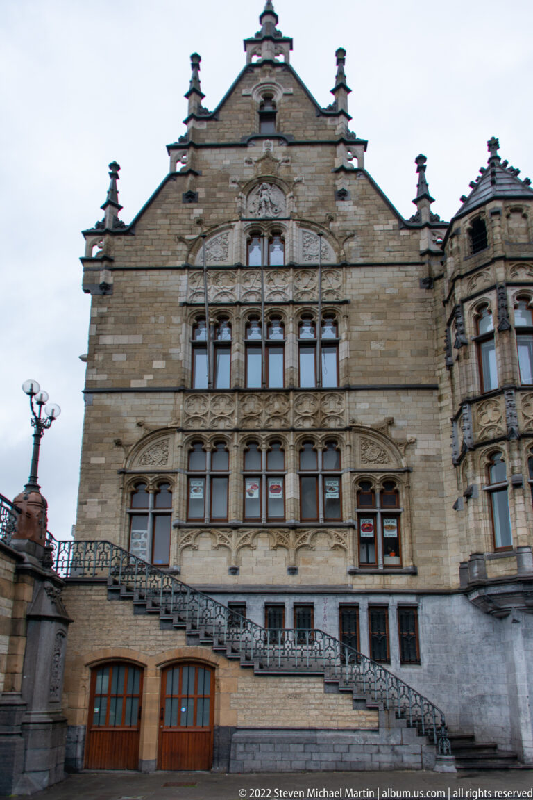 Symmetrical pale stone civic façade with mullioned windows, sculptural carving, stepped gable, and exterior staircase.