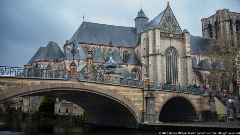 Saint Michael's Church in Ghent rising behind the broad stone arch of Saint Michael's Bridge.