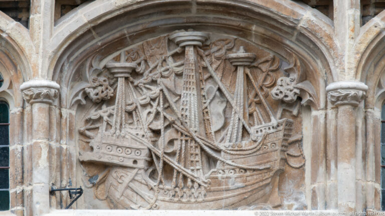 Stone relief of a multi-masted sailing ship with rigging and furled sails inside a carved arched niche.