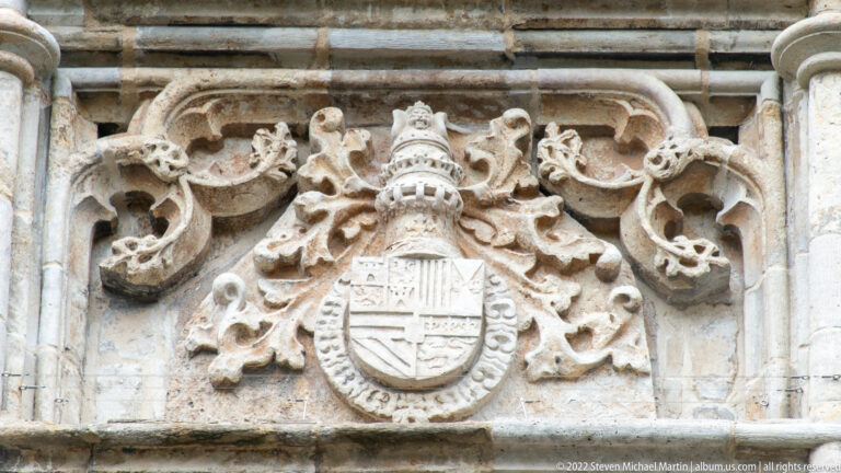 Crowned heraldic shield in carved stone with scrolling ornament and symmetrical supporters.