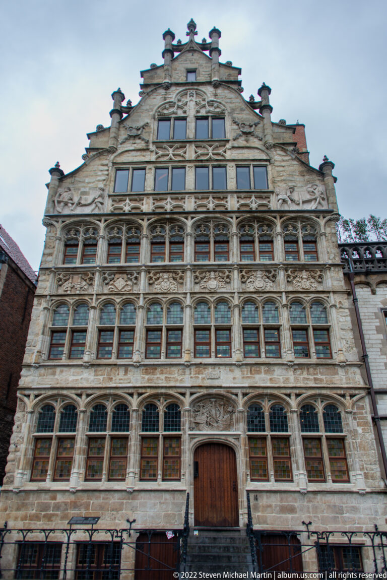 Tall ornate stone façade with stepped gable, rows of mullioned windows, arches, and dense sculptural decoration.