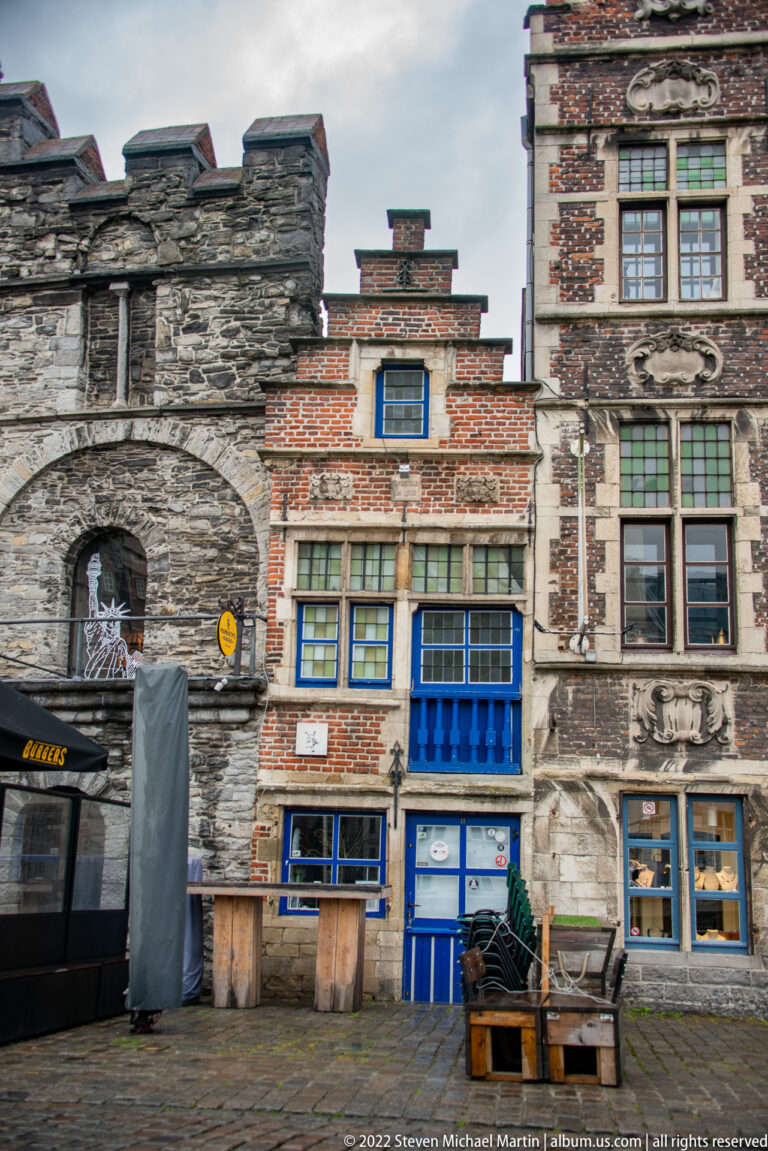 Low historic brick building with stepped roofline and blue doors beside rough stone masonry on a cobbled quay.