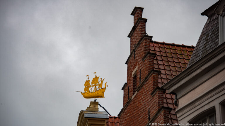 Golden sailing-ship finial silhouetted above red-tiled roofs and stepped brick gables.