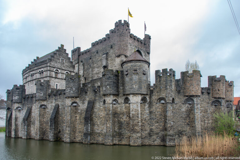 Gravensteen castle in Ghent with crenellated walls, round towers, central keep, and moat in the foreground.