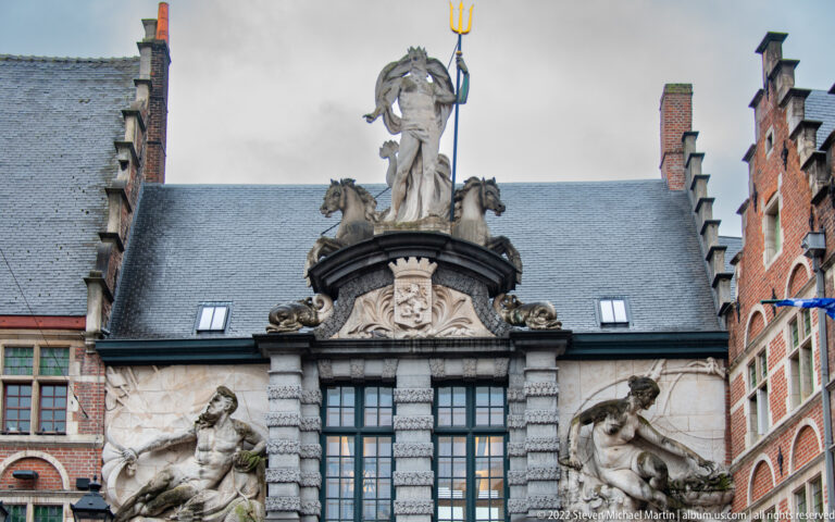Neptune with a golden trident and sea creatures crowning the ornate entrance façade of Ghent's Old Fish Market.