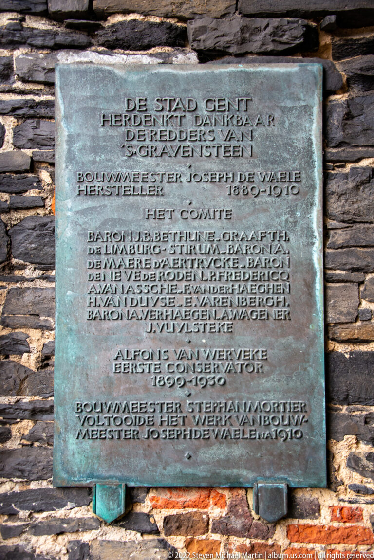 Green-patinated bronze commemorative plaque with Dutch text mounted on a dark brick wall.