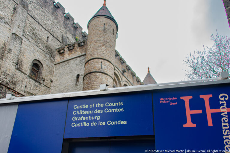 Blue multilingual Castle of the Counts sign below a round crenellated stone tower at Gravensteen.
