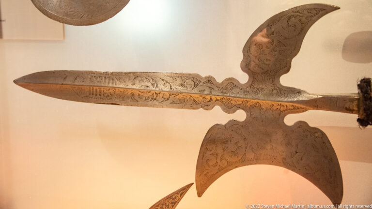 Ornately etched polearm head with a long central point and large curved side blades.