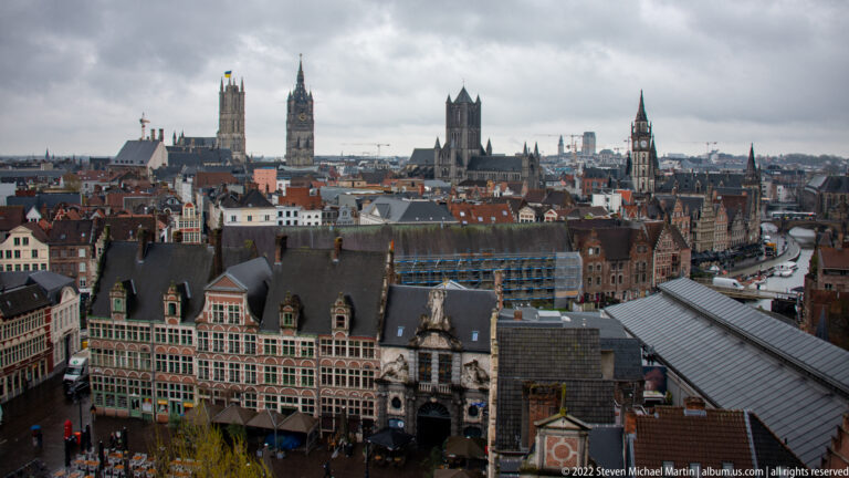 Elevated panorama of Ghent with historic roofs and façades in front of multiple church and civic towers.