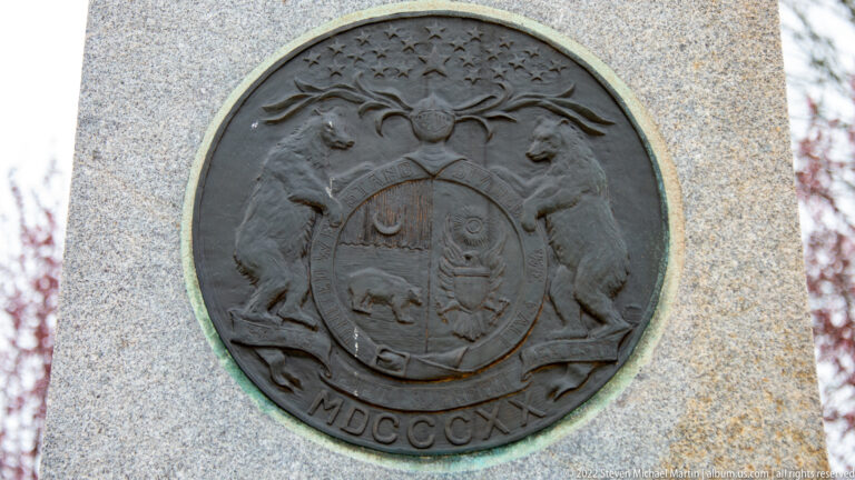 Round bronze Missouri state seal with two bears, central shield, and MDCCCXX mounted on granite.