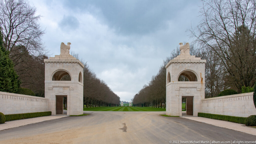 Paired stone gatehouses topped by eagles flank the road entering Meuse-Argonne American Cemetery.
