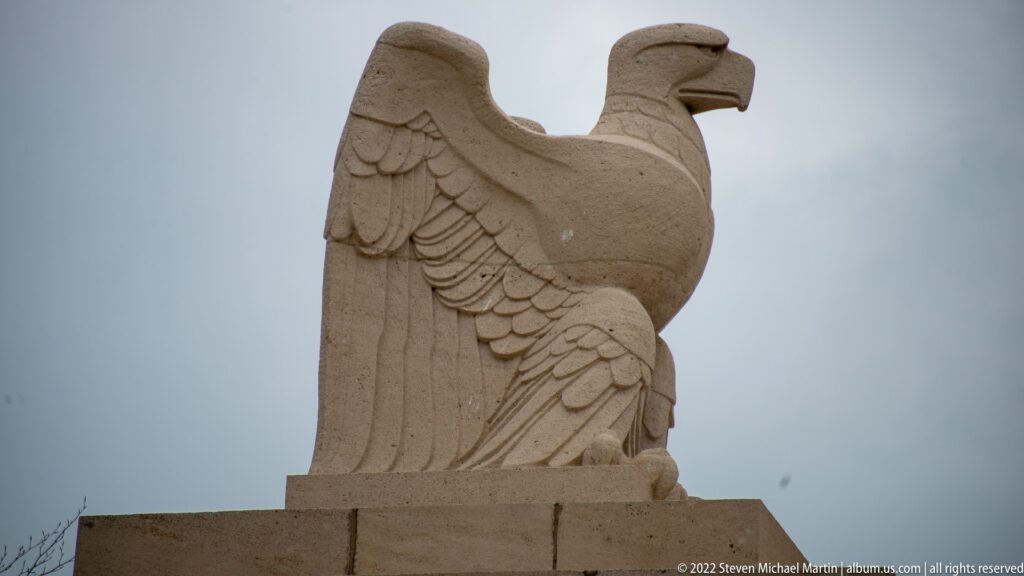 Profile view of a carved stone eagle standing on top of a cemetery entrance gatehouse.