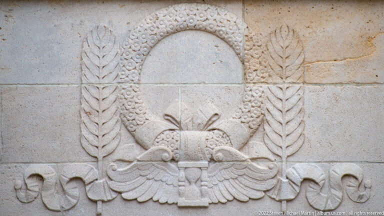 Stone relief of a circular wreath above an American eagle, flanked by laurel branches and ribbon carving.