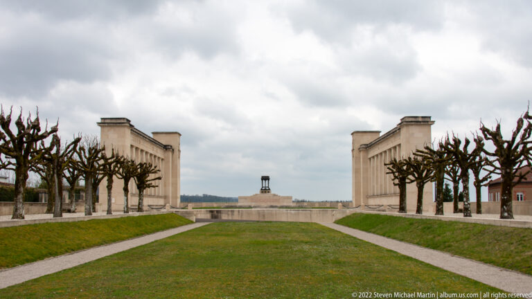 Symmetrical stone memorial structures flank a lawn and paths leading toward a smaller central monument.