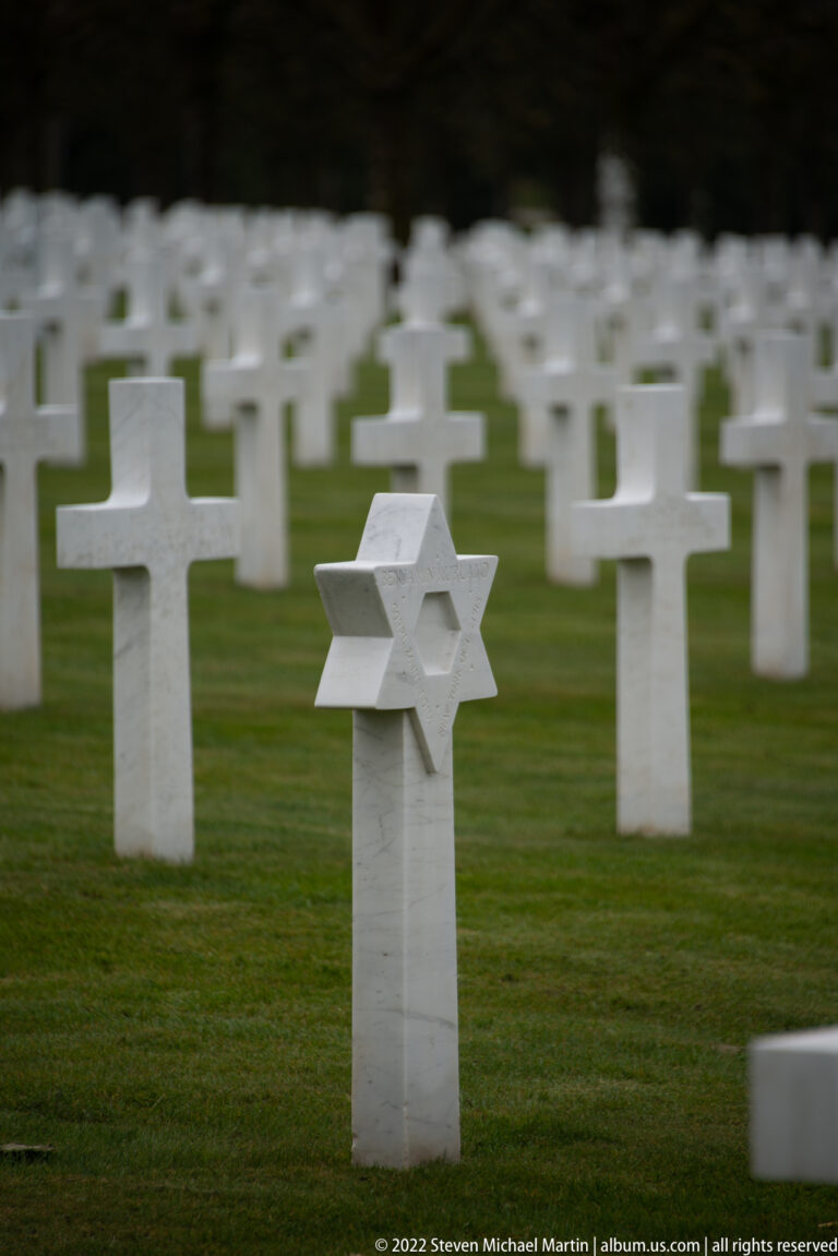 White Star of David grave marker stands among rows of white Christian crosses on the cemetery lawn.
