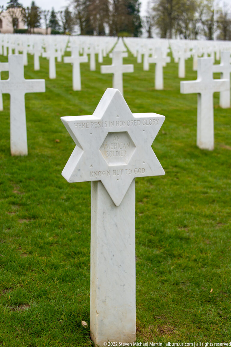 Star of David headstone for an unknown soldier stands among rows of white crosses.