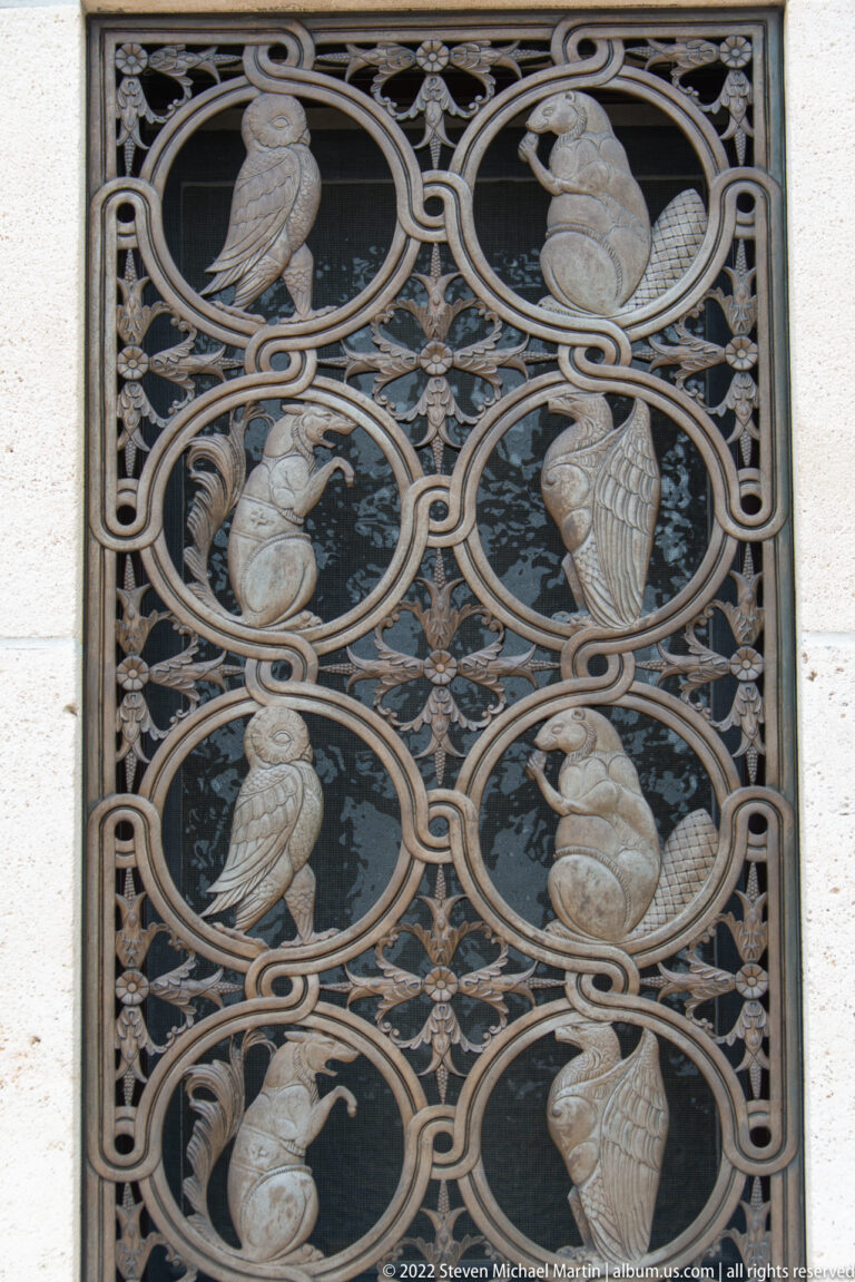 Close-up of ornate metal grille with stylized birds and other animals enclosed in circular medallions.
