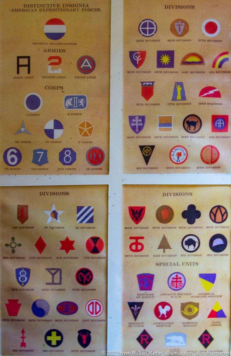 Wall display with rows of colorful American corps and division insignia, each labeled beneath its symbol.