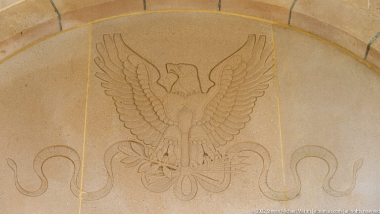 Incised spread-wing American eagle above a looping ribbon design on pale stone.