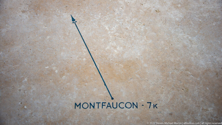 Blue arrow and inscription on pale stone point toward Montfaucon, seven kilometers away.