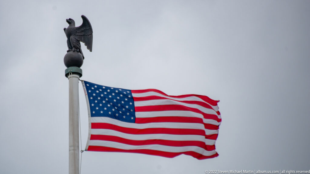 United States flag waves from a tall pole against a gray overcast sky.