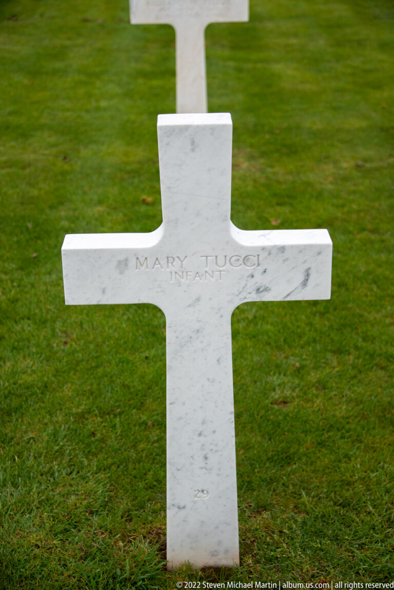 White marble cross inscribed with the name Mary Lucel and 1st Army, standing on green grass.