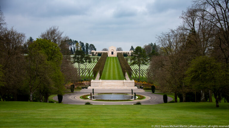 Elevated view over a circular fountain and formal lawns toward rows of graves and the distant memorial chapel.