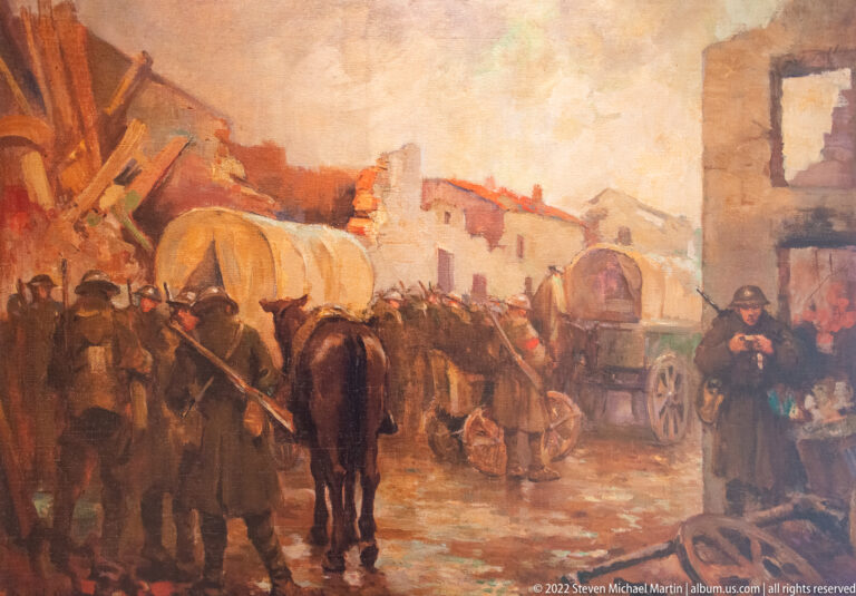 Painting of horse-drawn military wagons and soldiers passing through a damaged village street.