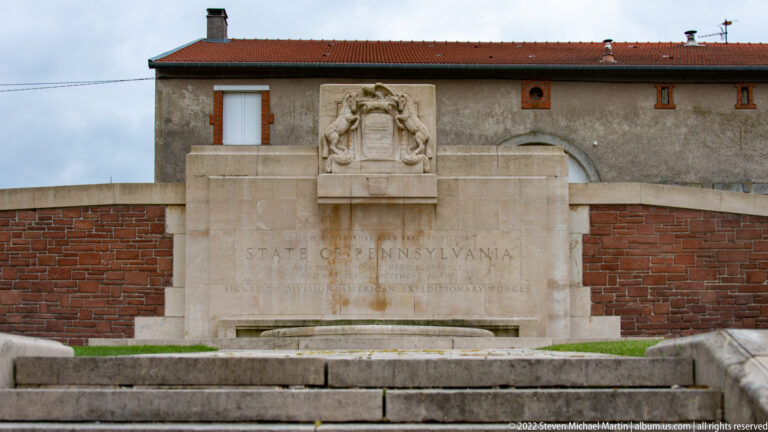 Stone Pennsylvania memorial with carved state emblem, inscription, steps, and a shallow basin before it.
