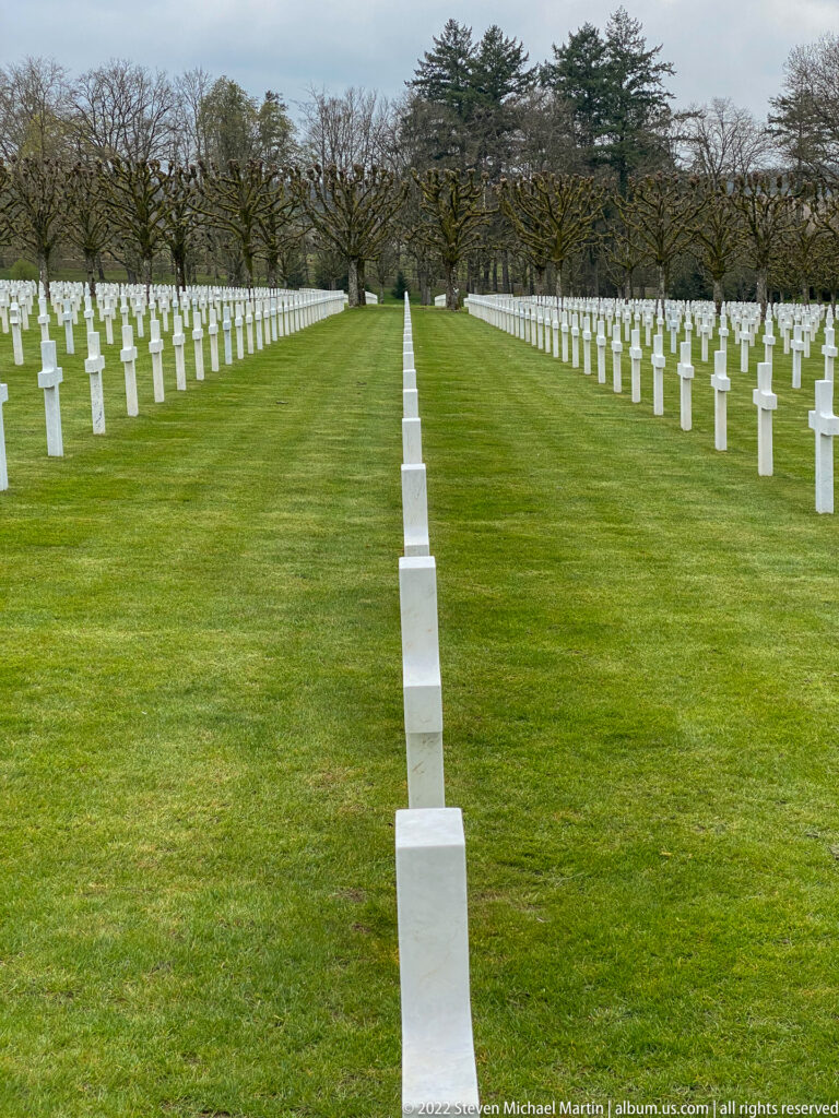 Straight row of white grave markers runs toward the horizon with parallel rows on both sides.